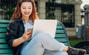 Woman on a park bench working on her phone and laptop